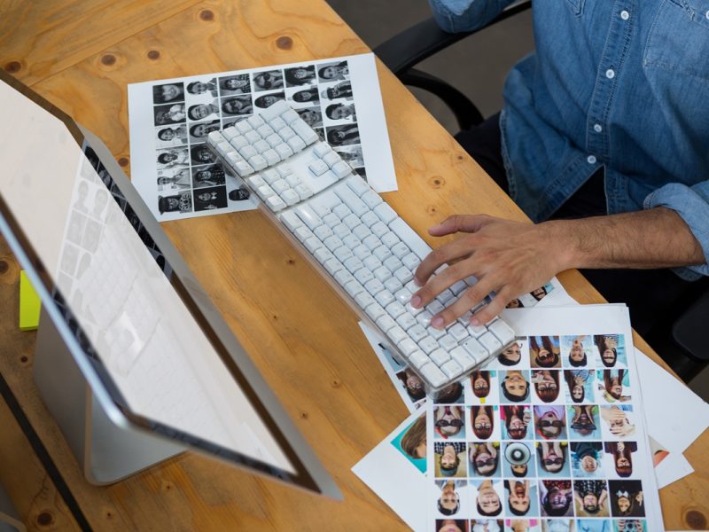 Man sitting with photographs and working on desktop pc in office